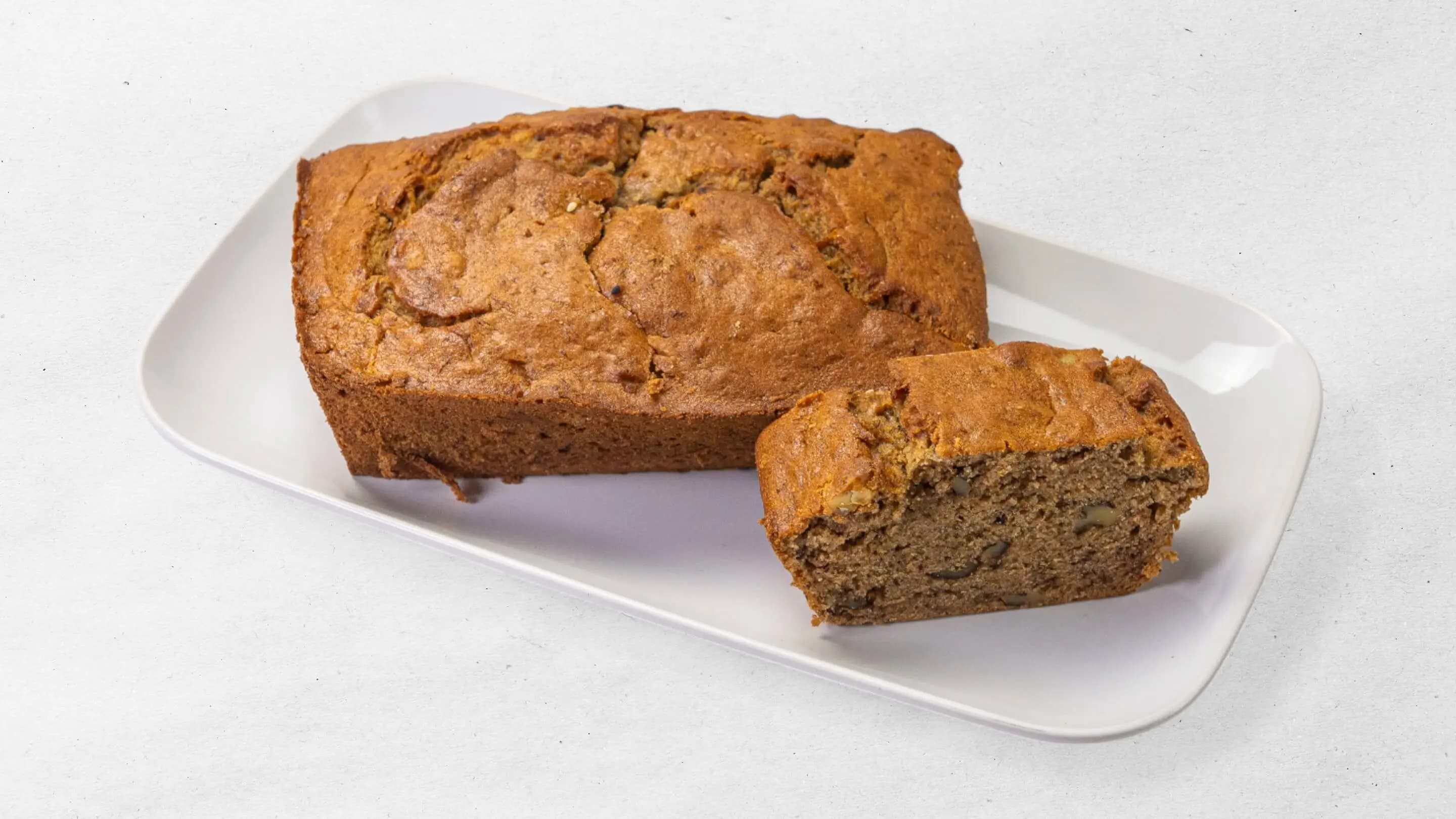 Homemade banana bread with walnuts, served sliced on a white plate