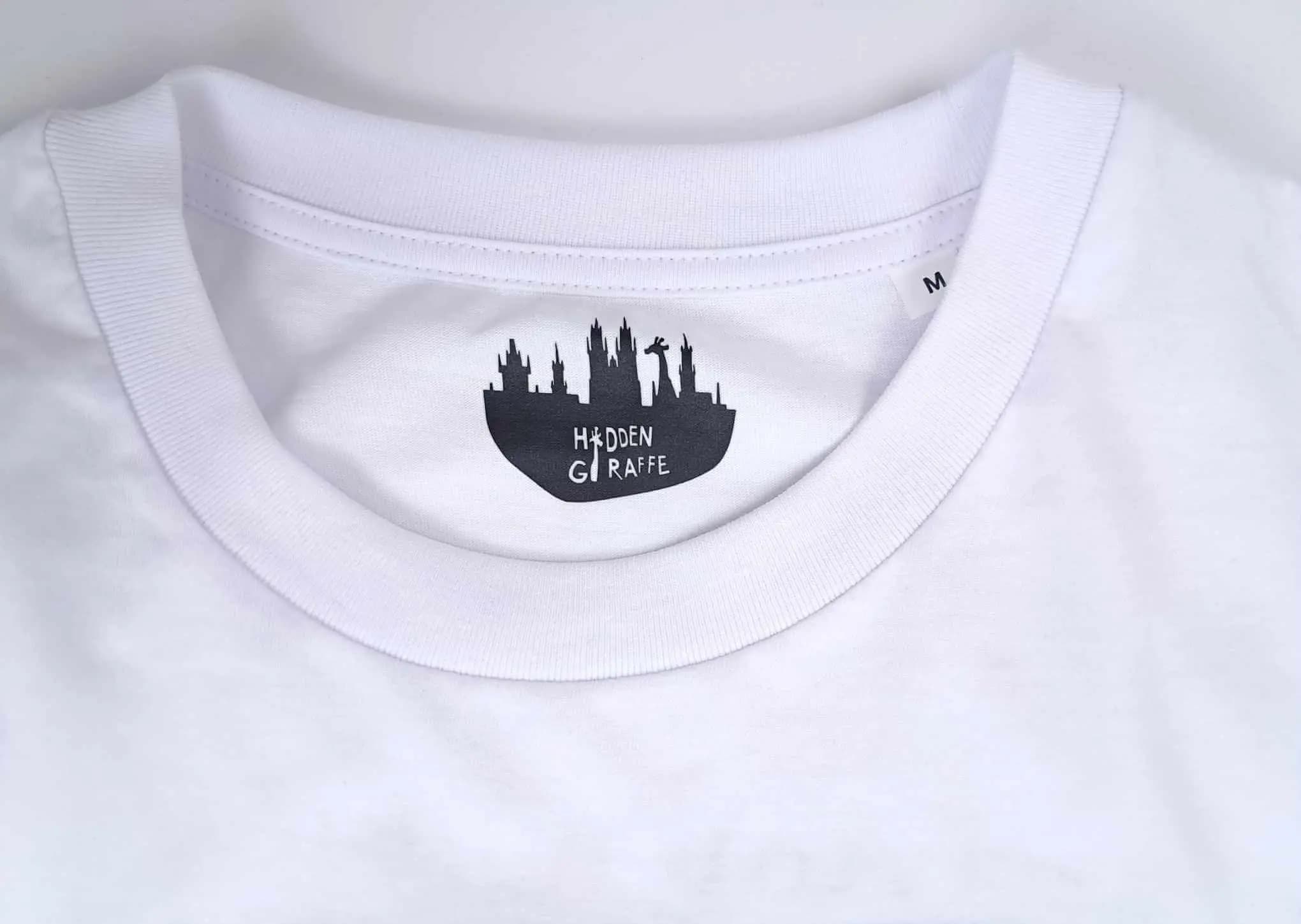 Close-up of the collar of a white T-shirt with the black Hidden Giraffe logo and size M label.