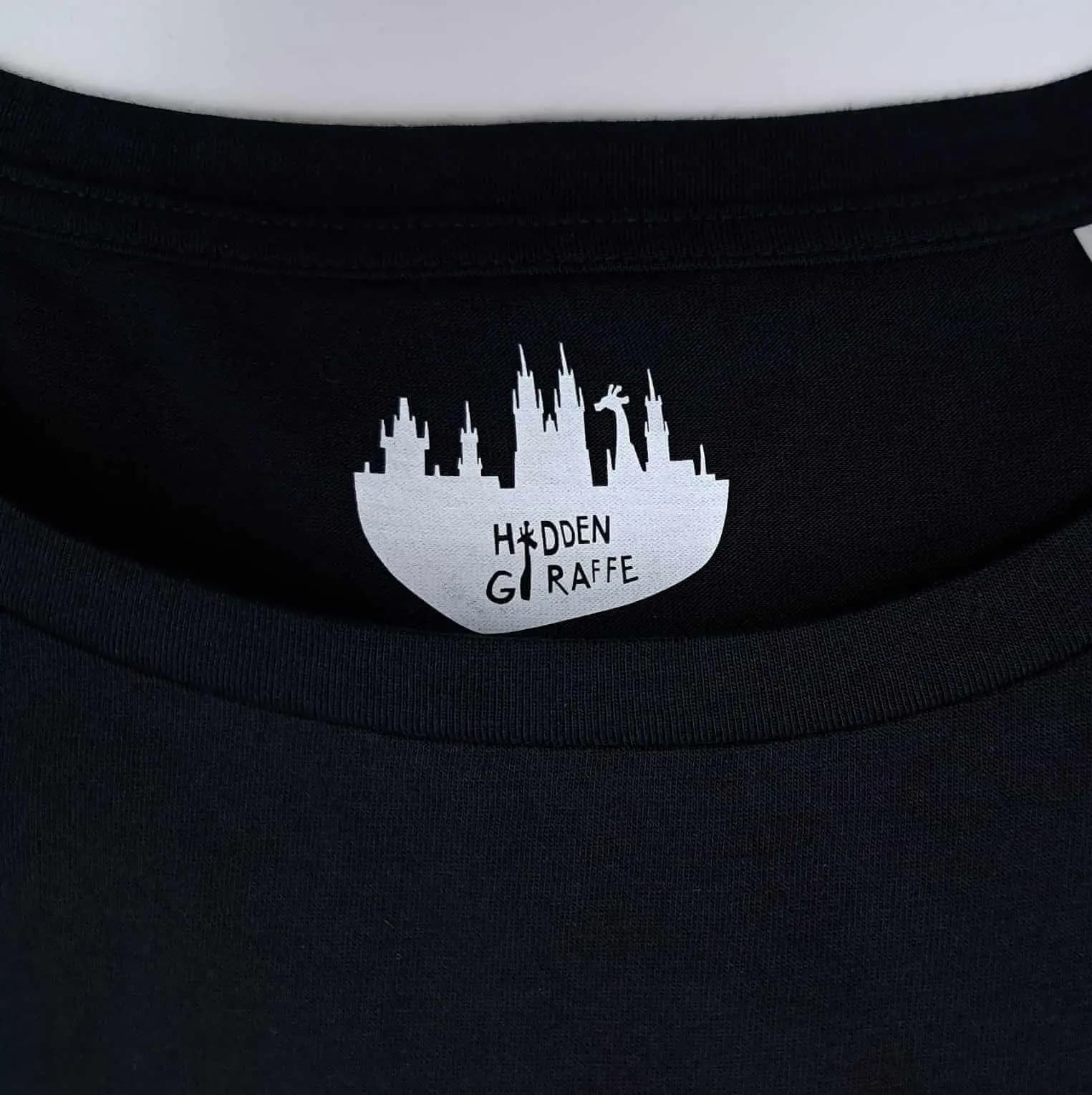 Close-up of the collar of a black T-shirt with the white Hidden Giraffe logo printed inside.