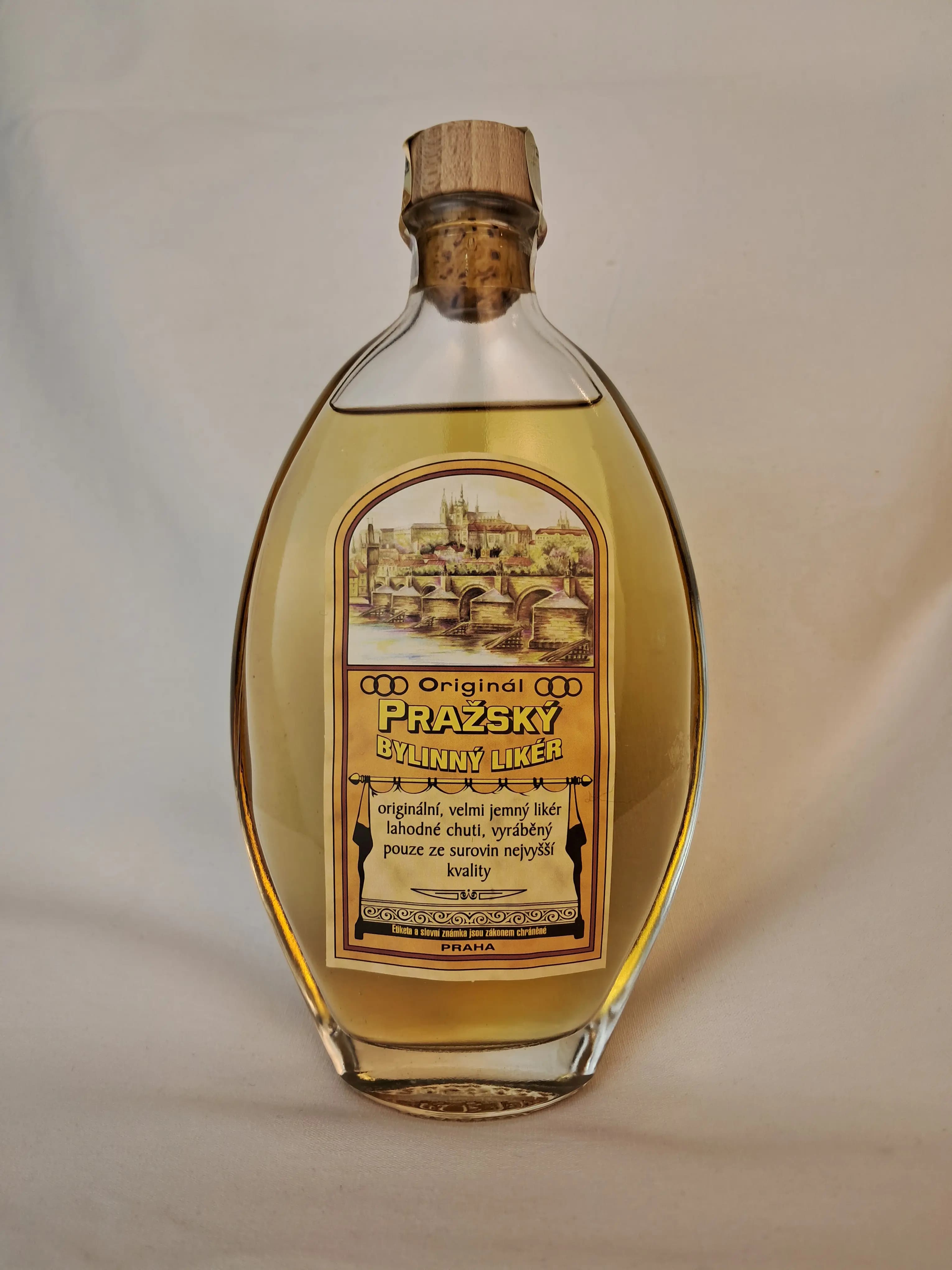 Bottle of Original Prague Herbal Liqueur with a wooden cap and an illustrated label featuring Prague Castle and Charles Bridge.